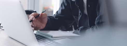 A man typing on a computer with a pen in his hand